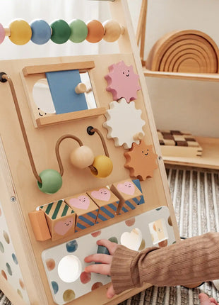 A baby explores sensory development while playing with the Tiny Land® Versatile Natural Wooden Baby Walker, which features colorful beads, gears, and shape blocks on a striped rug with wooden toys and shelves in the background.