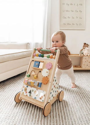 A baby pushes the Tiny Land® Versatile Natural Wooden Baby Walker, featuring colorful beads and gears to boost sensory development and fine motor skills, across a bright living room with a sofa, toys, and a striped rug.