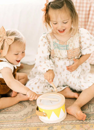 Two young girls sit on a patterned rug, smiling and playing together with the Tiny Land® Montessori Complete Baby Set (0-24 months). Colorful toys, crayons, and a book nearby enhance their sensory play. Both wear bows and light outfits.