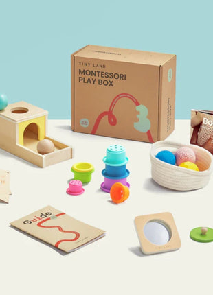 The Tiny Land® Montessori Complete Baby Set (0-24 months) includes a wooden toy with balls, stacking cups, colorful knitted balls, a guide booklet, cards, a mirror, wooden disc, and the book Body—all neatly arranged.