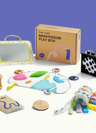 The Tiny Land® Montessori Complete Baby Set (0-24 months) includes a play box, mirror, wooden rattle, and sensory mat—perfect for sensory play and fine motor development—all displayed on a white surface with a purple background.